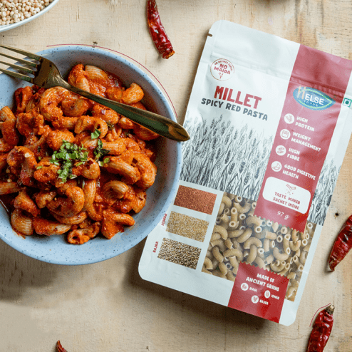 Helse Foods Spicy Millet Macaroni Pasta in a Bowl with fork and its Packaging on the side on a table